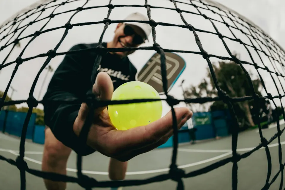 A smiling player holding a ball through the net
